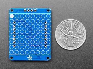 Back of blue, rectangular 8x8 LED matrix backpack add-on board next to US quarter for scale.