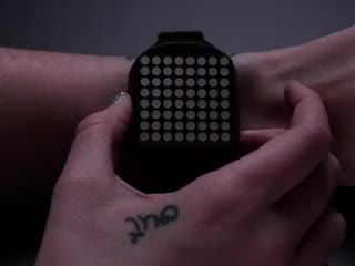 Hand pressing side of a square watch and time scrolls by on red LED matrix.
