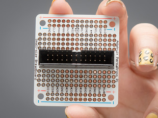 A white manicured hand holds up an assembled Adafruit Small-Size Perma-Proto Raspberry Pi Breadboard PCB.