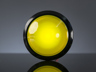 Head-on shot of illuminated massive yellow 100mm arcade button.