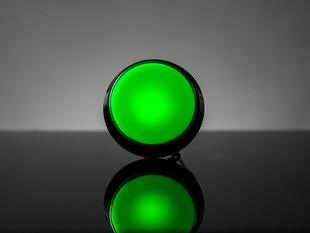 head-on shot of illuminated large green arcade button with LED.