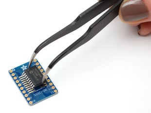 A pair of tweezers holding a SOIC chip hovers over the SMT Breakout PCB for SOIC-20 or TSSOP-20.