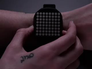 Hand pressing side of a square watch and time scrolls by on orange LED matrix.