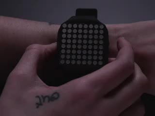 Hand pressing side of a square watch and time scrolls by on blue LED matrix.