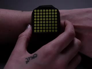 Hand pressing side of a square watch and time scrolls by on white LED matrix.