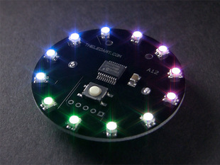 Angled shot of a black circular PCB ringed with LEDs glowing rainbow colors.