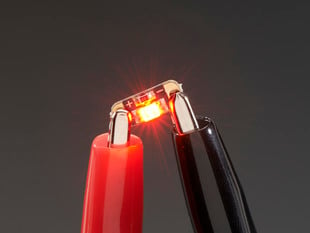 Single LED sequin PCB attached to two alligator clips, glowing red