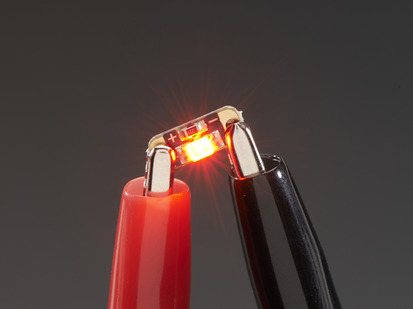 Single LED sequin PCB attached to two alligator clips, glowing red