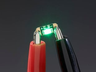 Single LED sequin PCB attached to two alligator clips, glowing green