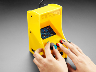 Two hands playing Cupcade with very small pacman game on display