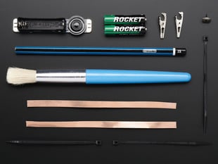 Collection of loose components in kit: assembled PCB, pencil, brush, copper tape and other parts.