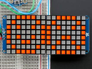Close-up of Soldered and assembled 16x8 1.2" LED Matrix + Backpack - Ultra Bright Square Amber LEDs on a breadboard. The LED Matrices display a smiling emoji and a frowning emoji.