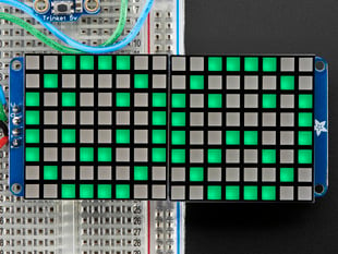 Close-up of Soldered and assembled 16x8 1.2" LED Matrix + Backpack - Ultra Bright Square Green LEDs on a breadboard. The LED Matrices display a smiling emoji and a frowning emoji.