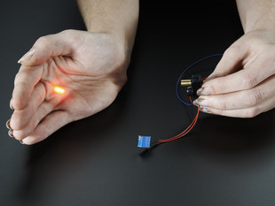One hand holding laser sensor, other hand blocking the laser output, with a red dot showing on palm.