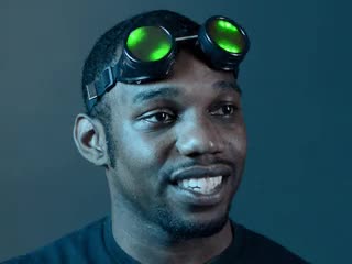 Video of a smiling Black man wearing LED goggles with swirling green LEDs.