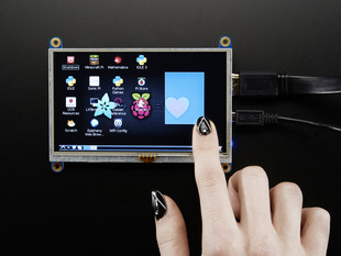 Black polished finger touching the display of a HDMI 5" Display Backpack. The HDMI screen displays a desktop image including the Adafruit logo, the Raspberry Pi logo, and a pink heart.
