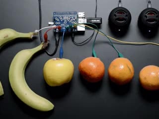 Video of a white hand pressing various bananas, oranges, and other fruits connected to a Raspberry Pi with Adafruit Capacitive Touch HAT via alligator test clip leads.