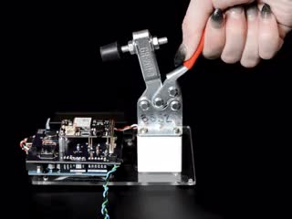 Video of a white hand manipulating a toggle clamp to press a PCB onto a prototype tester with pogo pins.