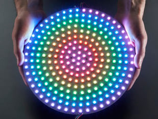 Two white hands holding a rainbow pulsing DotStar RGB LED Disk - 240mm diameter.