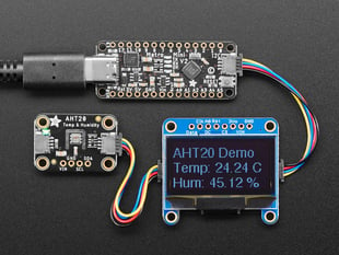 Overhead shot of long skinny black microcontroller connected to an OLED screen and a temperature-and-humidity sensor. The sensor data displays on the OLED.