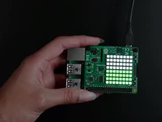 Video of a white hand tilting a  Raspberry Pi Sense HAT stacked on a Raspberry Pi. As it tilted back the LED's start to light up green. 
