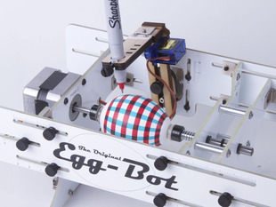 An intricate robot drawing a plaid design onto an egg with a sharpie pen.