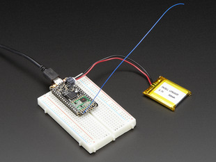Angled shot of a rectangular microcontroller connected to a white breadboard and a lithium battery. 