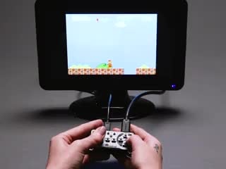 Video of a white hand playing a DIY gaming console on a small monitor.