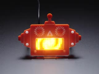 An assembled orange robot head displaying yellow swirls from its mouth. 