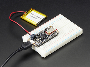 Angled shot of rectangular microcontroller on white breadboard connected to a battery.