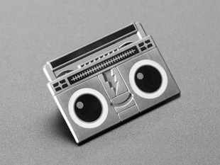 Angled shot of an enamel pin resembling a wide-eyed boombox cartoon character. 