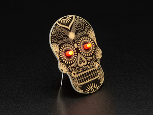 Angled shot of a Dia de los Muertos skull PCB with red glowing LEDs for eyes.