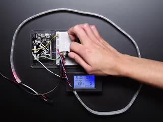 Video of a white person's hand turning a knob assembled on a breadboard with a microcontroller and a digital power meter. As the knob is turned, an LED strip lights up along the strip, and the power meter displays the voltage, current, etc.