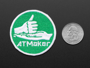 Circular embroidered badge with hands motioning for Rock with the words AT MAKER in white, over a green background. 
