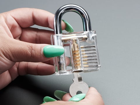 Hands holding clear padlock and opening with a small key.