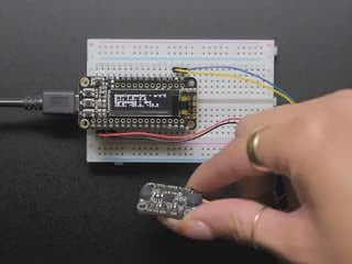 Video of a white hand moving a sensor around that connected to an OLED and white breadboard.
