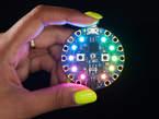 shot of a Black woman's neon-green manicured hand holding up a Circuit Playground Bluefruit glowing rainbow LEDs.