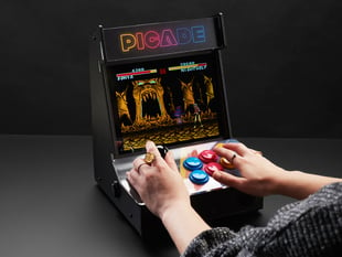 Angled shot of a Pimoroni Picade Cabinet Kit being played by a set of white hand. 