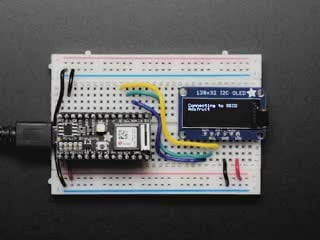 Adafruit AirLift Bitsy Add-On – ESP32 WiFi Co-Processor connected to a half sized white breadboard and a OLED with various wording showing on the display. 