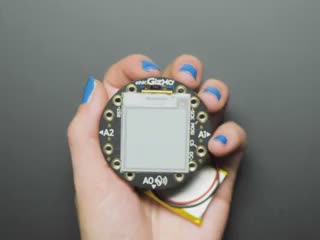 Hand holding E-Ink gizmo bolted onto PCB, refreshing itself