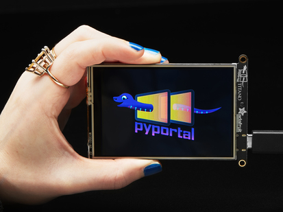 Hand holding PyPortal Titano development board with SAMD51, ESP32 Wifi, and 3.5" touchscreen TFT display.