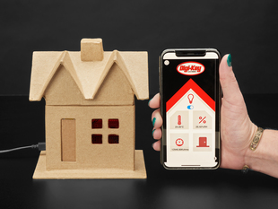 Assembled cardboard house next to a hand holding up a smart phone displaying a DigiKey app.