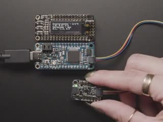 Video of a white hand moving a sensor around that connected to an OLED and a blue rectangular board. 