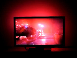 Large flatscreen TV with red-tinted scene and red LEDs lighting wall behind it.