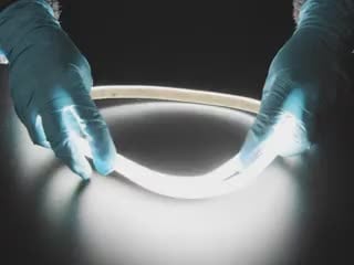 Two hands repeatedly bending and manipulating lit-up bright white flexible LED strip.