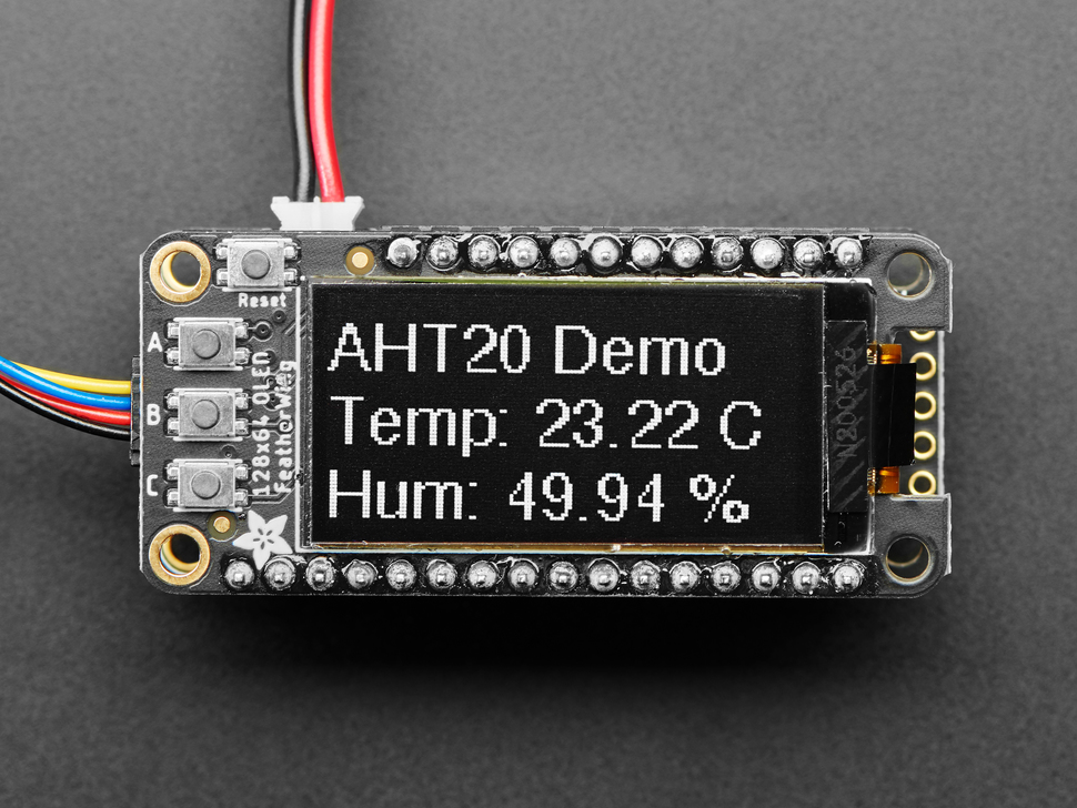 Close up of a Adafruit FeatherWing OLED - 128x64 OLED Add-on For Feather - STEMMA QT / Qwiic. Display reads "AHT20 Demo, Temp:23.22C, Hum: 49.94%"