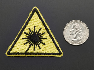 Triangle shaped yellow embroidered badge with laser symbol next to quarter for scale