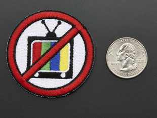 Circular badge with an image of a television crossed out with red line, next to a quarter for scale