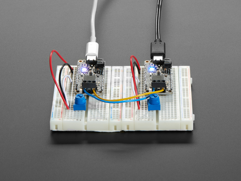 Angled shot of  2Adafruit Feather M4 CAN Express with ATSAME51 on white breadboards side by side. 