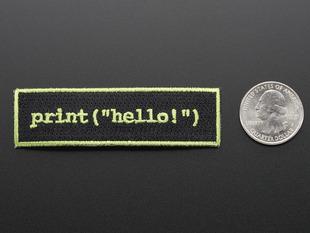 Rectangular embroidered badge with yellow words print hello on black background with yellow edging and a quarter for scale. 